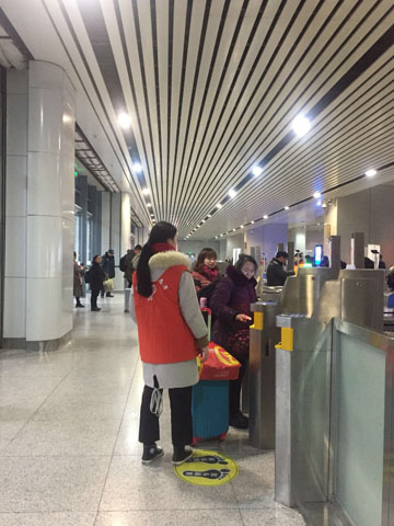 帮助旅客使用人脸识别系统检票的志愿者    画外:重庆北站进站口,在